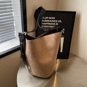 Retro brown suede bucket bag for women with wide black shoulder strap on a sleek metal table