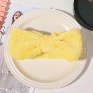Close-up of a soft yellow coral fleece headband with a large bow for skincare routines
