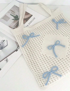Detailed close-up of ivory hollow knit tote bag featuring blue knitted bow accents