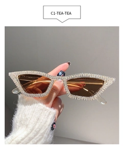 Detailed view of cat eye sunglasses with silver rhinestones and brown lenses held by hand