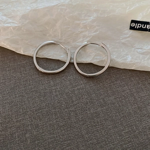 Close-up of polished silver hoop earrings on a textured minimalist background