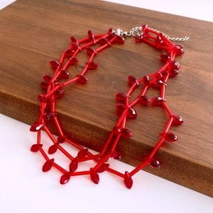 Close-up of a layered red beaded necklace with faceted waterdrop pendants on a wood base