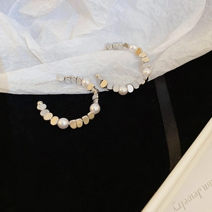 Close-up of C-shaped silver hoop earrings featuring alternating white pearls and flat discs