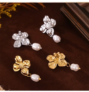 Detailed top view of gold and silver flower-shaped earrings with teardrop pearls on velvet