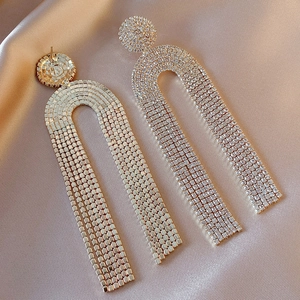 Detailed close-up of gold U-shaped tassel earrings with rhinestones on silk