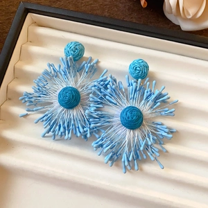 Close-up of blue woven flower earrings with radiant texture for beach vacation style