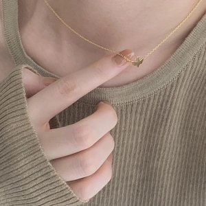 Close-up of a delicate gold bird pendant necklace worn on a beige knit sweater
