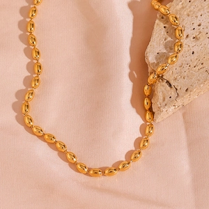 Detailed macro view of 18K gold plated oval bead chain necklace on marble stone