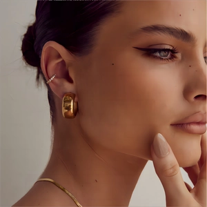 Close-up of golden C-shaped wide hoop earring and small ear cuff on female model