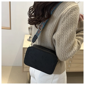 Detail of black embossed floral square bag with a wide colorful woven shoulder strap