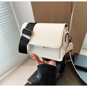 Detail of a minimalist cream-colored crossbody bag with wide black shoulder strap