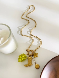 Artistic detail of a gold chain necklace with grape and cowboy boot charms on white background