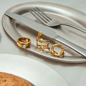 Detailed view of three gold-plated lava-style rings with white pearl on a silver platter