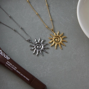Flat lay of gold and silver sun pendant necklaces with hammered texture on stone surface