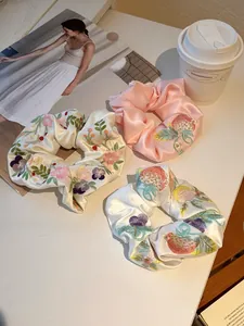 Detailed close-up of three satin scrunchies featuring intricate floral and berry embroidery