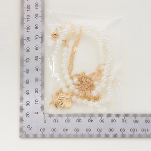 Close-up of pearl necklace with gold starfish and shell pendants showing size with a ruler