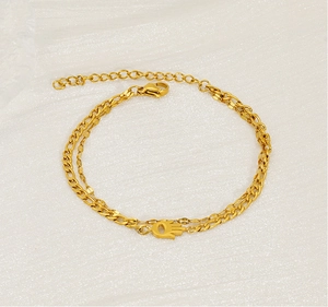 Detailed shot of double-layer gold Hamsa Hand charm bracelet on white textured fabric