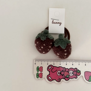 Pair of knitted strawberry hair ties in dark brown with green leaves and size ruler