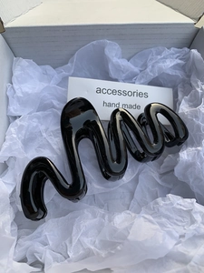Detailed view of a gloss black wave hair claw clip inside an aesthetic white gift box