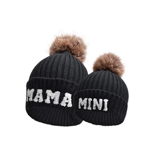 Dettaglio di berretti in maglia neri con ricamo MAMA e MINI e pompon in finta pelliccia