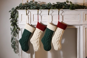 Detail of four cable knit Christmas stockings hanging on a festive decorated fireplace