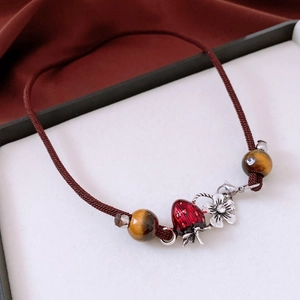 Detail of tiger eye beads with red strawberry enamel charm on brown braided necklace