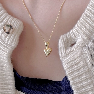 Close-up of a minimalist gold heart pendant necklace on a beige knit cardigan
