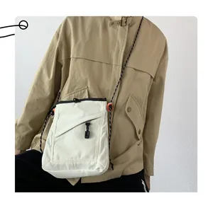 Detailed shot of white canvas crossbody bag with orange toggle and woven strap on model