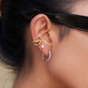 Close-up of gold ear cuff, textured silver hoop and round diamond stud earring set
