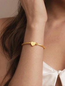 Detailed view of twisted gold rope cuff bracelet with a polished heart pendant on wrist