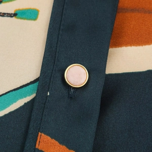 Close-up of pink button with gold trim on geometric print silk-like fabric blouse