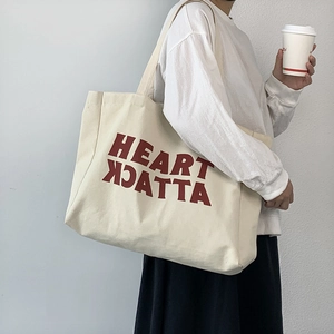 Canvas tote bag with red Heart Attack print shown on shoulder for size and fit perspective