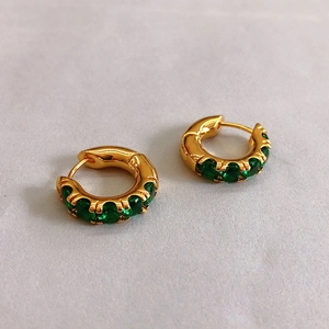 Detail of C-shaped golden earrings featuring green zircon stone inlay on a neutral background