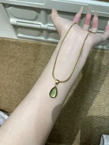 Detail of a green teardrop pendant on a gold snake chain worn on neck area