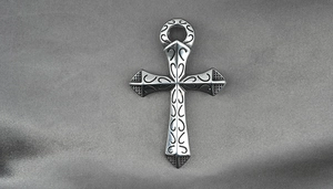Detailed view of silver cross pendant with intricate scroll patterns on silk background