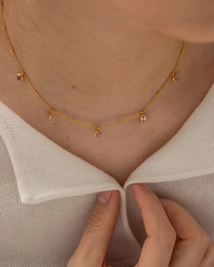 Vue détaillée d'un collier en titane doré avec des pendentifs en pierres roses rondes et carrées