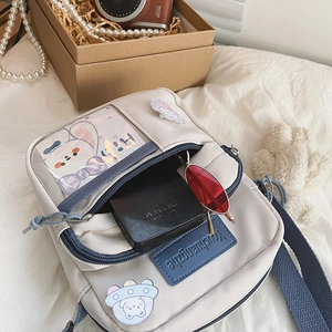 Détail du sac bandoulière en toile avec fenêtre transparente, écusson et sangle bleue