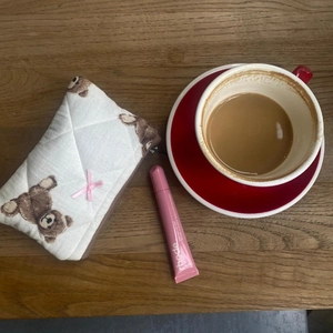 White quilted cosmetic bag with teddy bear pattern on wooden desk with coffee