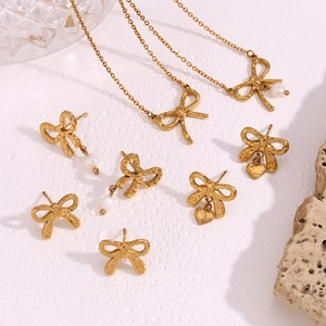 Detailed close-up of gold bow earrings and heart pendant necklace with pearls on white texture