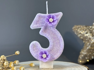 Detailed view of purple glitter number 3 candle with 3D floral accents on wood