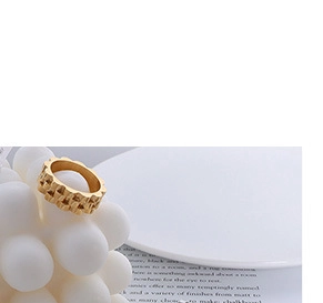 Détail d'une bague large dorée avec texture tissée irrégulière et motifs géométriques