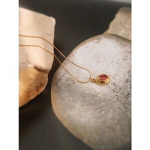 Close-up of gold plated necklace with oval ruby pendant on rustic stone display