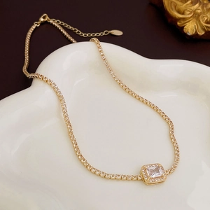 Close-up of golden necklace with square zircon pendant on a white wavy ceramic plate