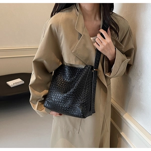 Detail of black woven leather tote bag with thick strap on model in trench coat