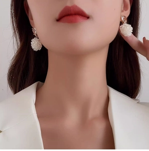 Detail shot of elegant white beaded flower drop earrings worn with a white blazer