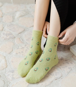 Close-up of green mink velvet socks featuring cute avocado patterns on a stone floor