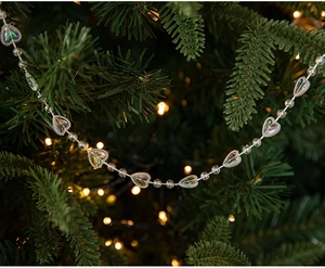 Detail of silver heart-shaped bead chain hanging on a Christmas tree with warm lights
