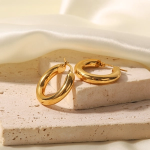 Polished chunky gold hoop earrings displayed on white silk and beige stone background