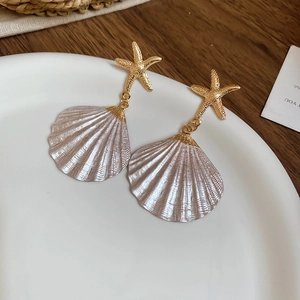 Detailed close-up of gold starfish and shell earrings on a white plate with rustic decor