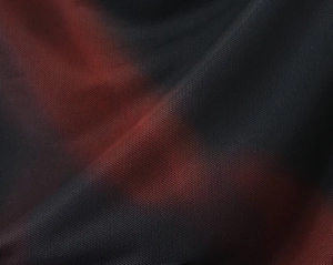 Dettaglio macro del tessuto a maglia fitta con texture sfumata nero e rosso scuro